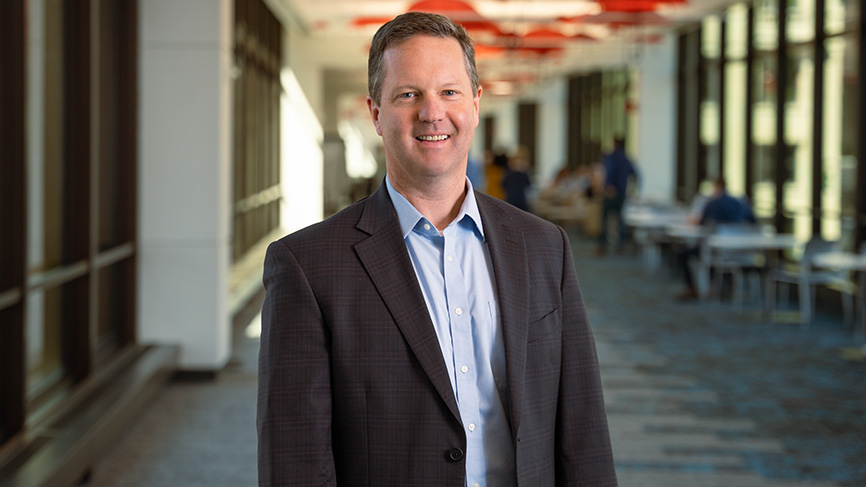 Smiling man in a business suit standing in a bright office hallway.