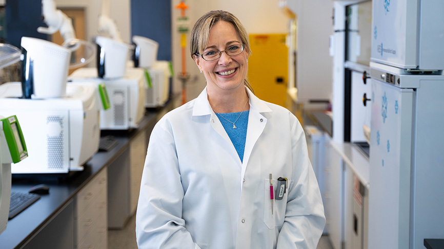Smiling woman in a lab coat standing in a laboratory.