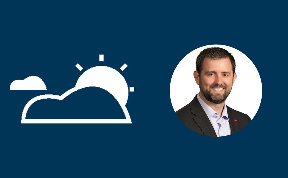 Professional headshot of a smiling man with dark hair and beard wearing a dark suit and light blue shirt, displayed in a circular frame. A white icon showing clouds and sun appears to the left against a dark blue background.