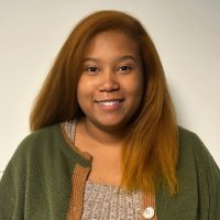 Professional portrait of Alexis Gill from Travelers Enterprise Billing & Receivables Management. She has long, wavy reddish-brown hair and displays a warm, genuine smile while looking directly at the camera. She wears a green or olive-colored blazer, photographed against a clean, neutral background.