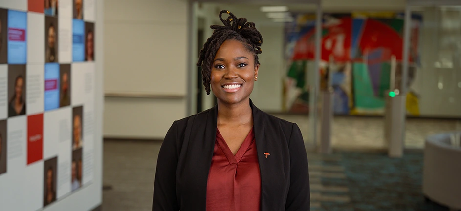 A young woman in a blazer smiles as she stands in a hallway
